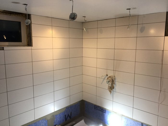 Halvfärdigt kakelarbete i ett badrum med oskyddade elledningar och en raggarhandske.