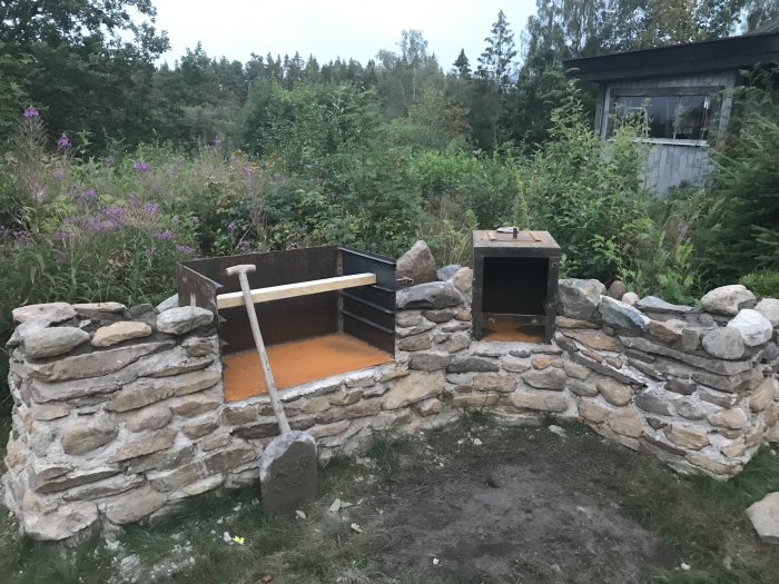 Byggprocess av en stengrill och rök i en trädgård med en cortenplåtsgrill och stenar lagda i rader.