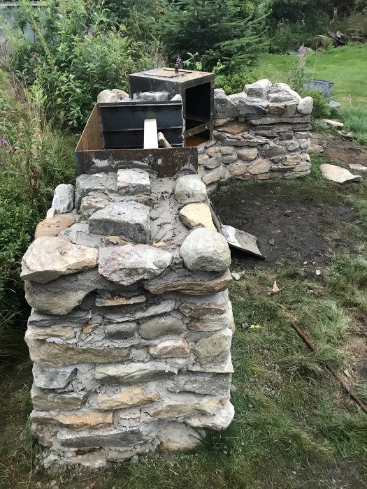 Egenbyggd stenmurad grill och rök med cortenplåtar i trädgård under konstruktion.