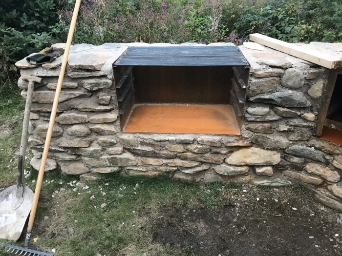 Stenbyggd grillstation under konstruktion med första lager sten och svetsad cortenplåt.