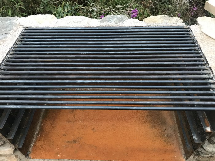 Självsvetsat grillgaller över cortenplåtseldlåda, inramat av stenar.