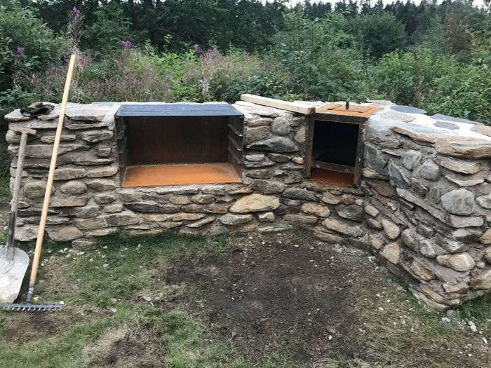 Halvfärdig stenmurad grill och rök med cortenstål insatta i en trädgård.