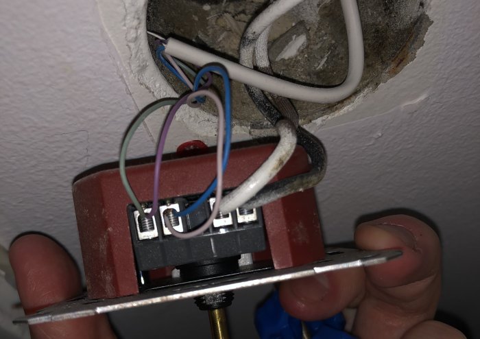 Närbild av en öppen väggdimmer med synliga kopplade kablar som hålls uppvisad av en hand.