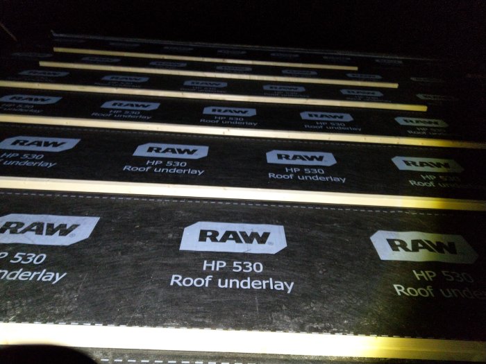 Reglar skruvade över skarvarna av svart takunderlagspapp märkt "RAW HP 530 Roof underlay".