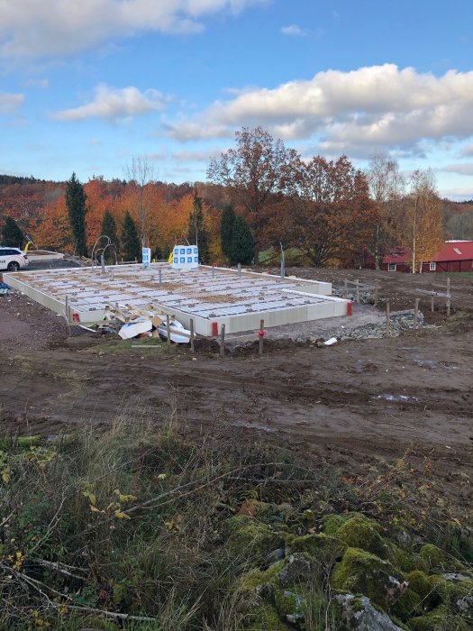 Grundläggning för husbygge med markarbeten klara och förberedelser för isolering samt kantstål vid garageportar.