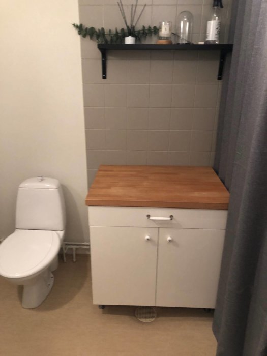 Radhus tvättstuga/toalett med kakelvägg, toalett och skåp, före renovering.