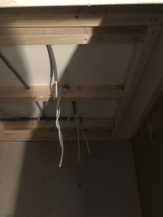 Elledningar dragna genom ett tak med synliga träbjälkar och flexrör för installation av downlights.