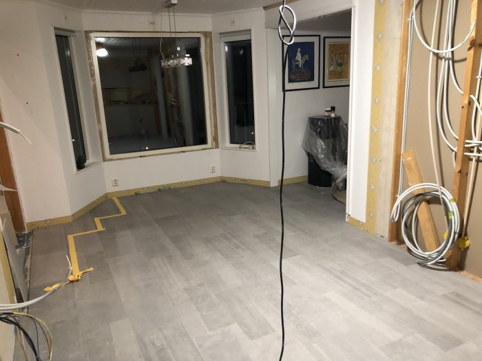 Delvis lagd hallplattor och nyinstallerat stort fönster i ett under renovering rum.