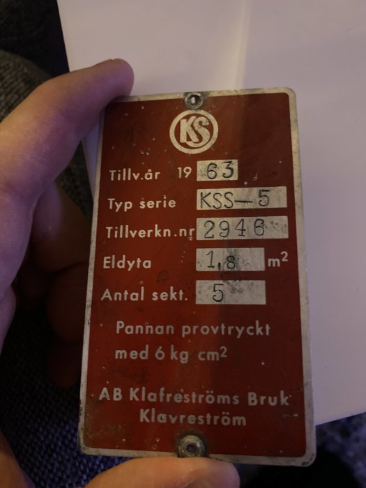 Hand håller en gammal röd skylt från AB Klafreströms Bruk med teknisk information från 1963.