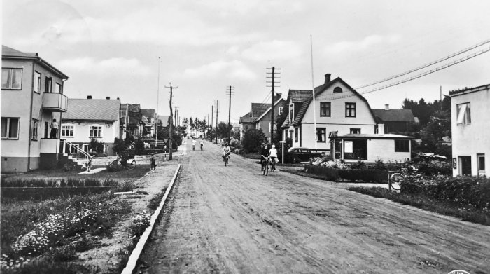 Svartvit historisk bild av en gata ca 1940 med krokiga elstolpar på vänster och raka telestolpar på höger.