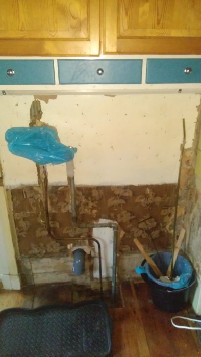 Vägg i gammalt hus med borttagna rör, synliga väggskivor och verktyg på golvet.