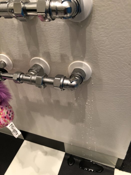 Läckage av vatten bakom vit ring på badrumsväggens rörinstallation.