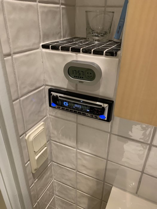 Vattenbeständig radio med tidsvisning monterad på kakelvägg i badrum.