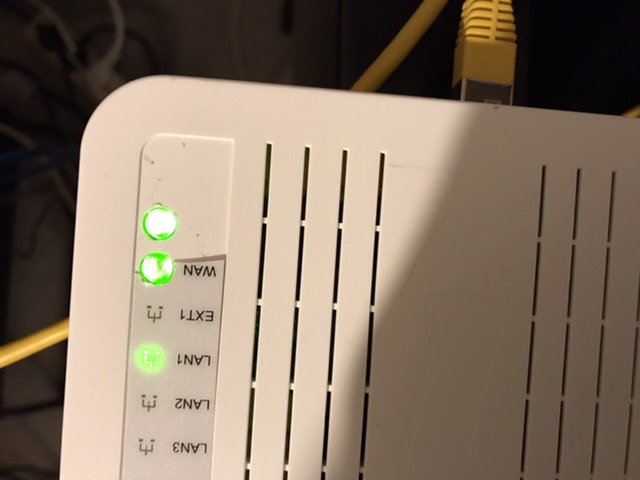 Nätverksutrustning med tända indikatorlampor, WAN LED lyser grönt och en gul nätverkskabel är ansluten.