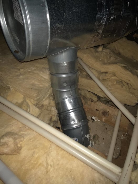 Ett metallrör för köksfläkt, ihopskarvat och oisolerat, i ett tak med synlig mineralullsisolering.