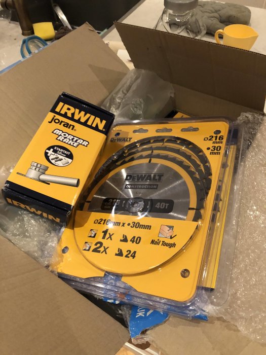 En ny Dewalt sänksågsklinga förpackad bredvid en IRWIN förpackning inuti en öppen kartong.