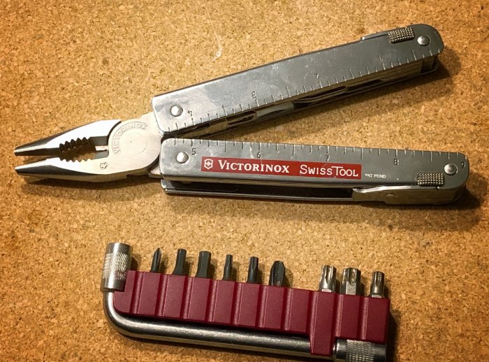 Victorinox SwissTool med tänger öppet och bitsats på korkbräda.