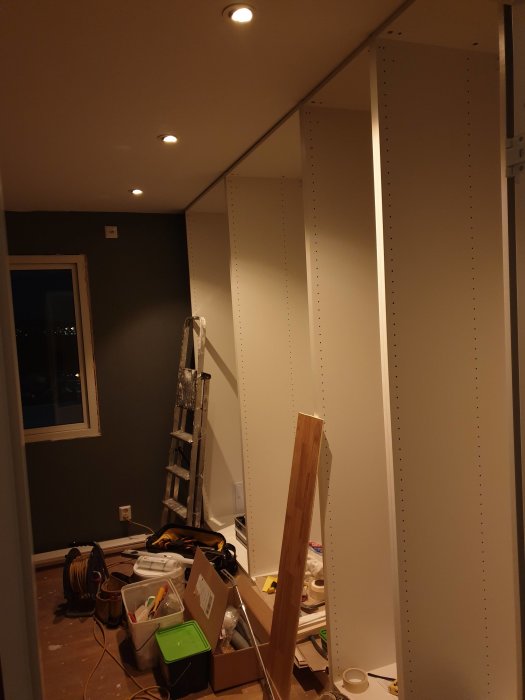 Oinreddt rum under renovering med osynliga kablar för lågspänningsmatning, stegar och byggmaterial.