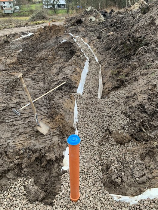 Grävd slinga för dränering fylld med makadam och en vertikal avloppsrör, vid byggprojekt.