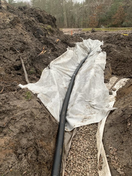 Grundarbete med makadam, geotextil och avloppsrör vid byggprojekt.