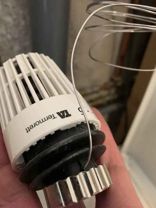 Närhandbild på en termostat på en radiator med en liten metallsladd ansluten, tydande på eventuellt tekniskt problem.