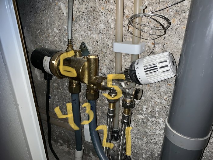 VVS-installation med varma och kalla stål- och plaströr markerade med gula pilar samt en termostat.