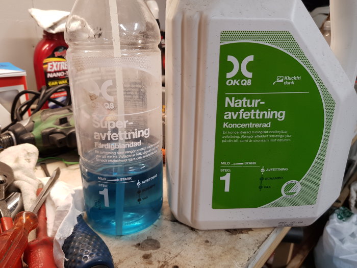 Två flaskor med avfettning för bilvård, en märkt 'Super-avfettning' och den andra 'Natur-avfettning', på en verktygsbänk.