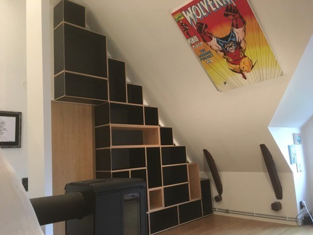 Bokhylla i svart linoleum och ek på vindsvåning med snedtak och inramad Wolverine-poster.