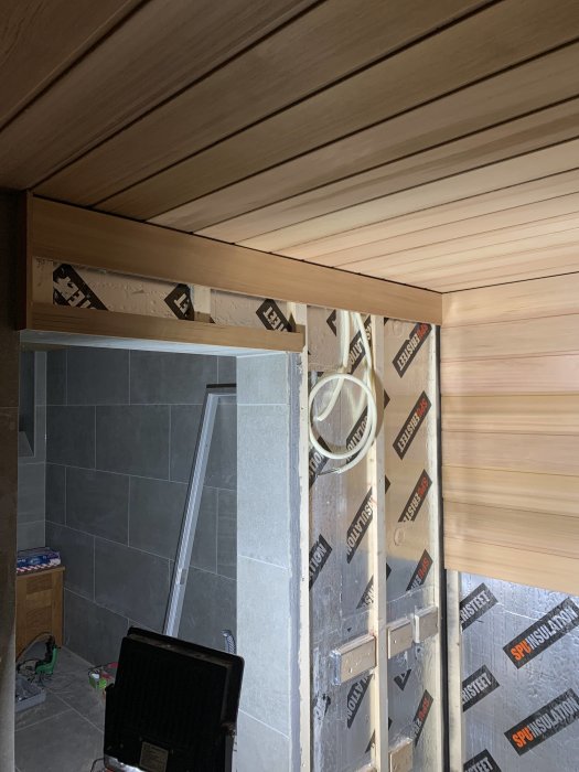 Installation av träpanel i taket bredvid en oisolerad vägg med synlig isolering och byggmaterial.