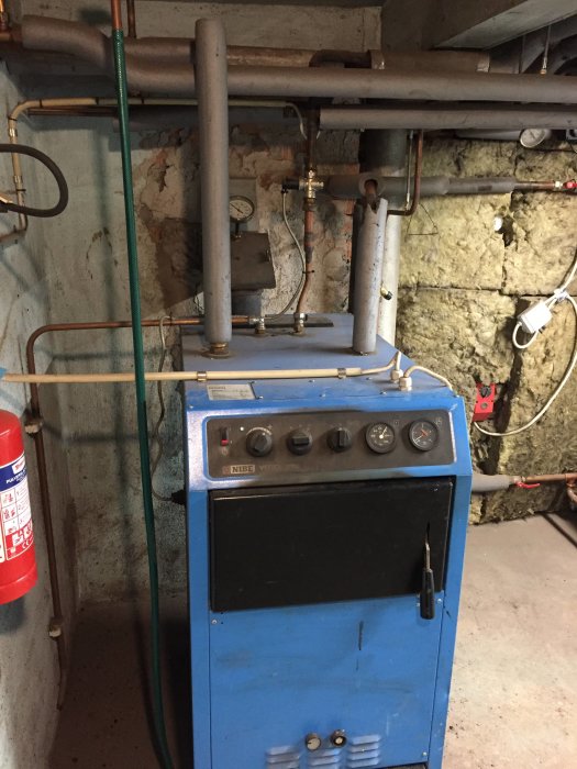 Ett vedeldat värmesystem av märket Nibe Vedex 3000 i en källare med kopparledningar och mätare ovanför pannan.