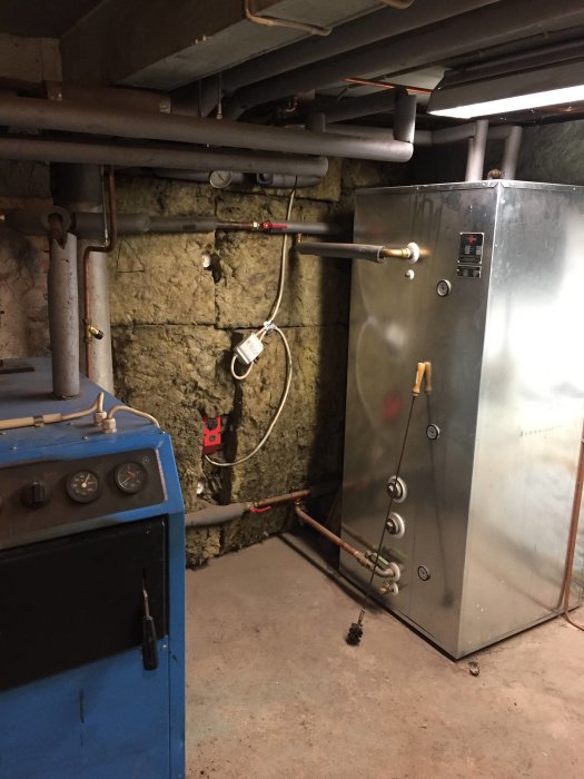Vedeldad panna och ackumulatortankar i en källare med synliga rör och ledningar.
