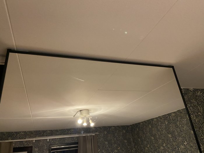 Nyinstallerad skjutdörr med 2 mm glipa nära taket, visar taklampa och tapetserad vägg.