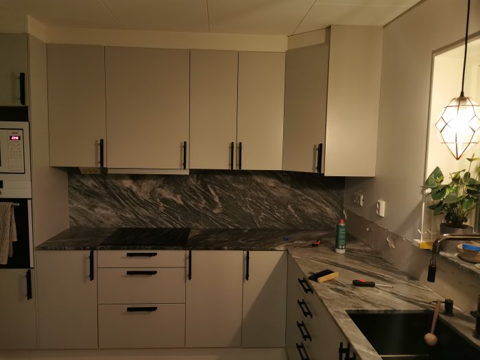 Kök under renovering med marmorliknande plattor på vägg, skåp och verktyg synliga.