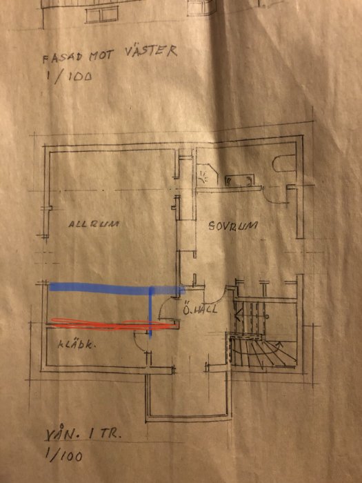 Arkitektritning av husplan med en befintlig vägg markerad i rött och en planerad ny vägg i blått.