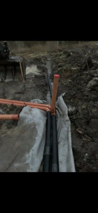 Dräneringsrör ledande under en grusväg med nylagd slinga fortsättande parallellt längs vägen i en utgrävd ränna.