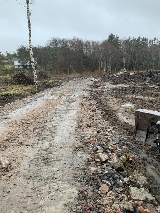 Grusväg under konstruktion med dräneringsslingor och högar av jord på sidorna i ett blött landskap.