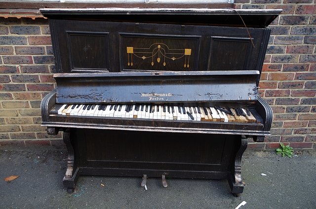 Gammalt upprätt piano med slitet utseende och delvis saknade tangenter.