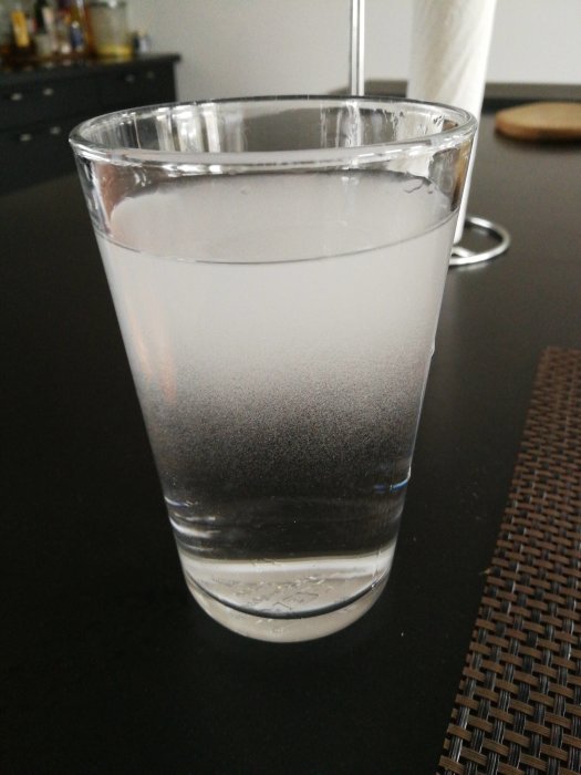Ett glas med vatten som är vitt och grumligt med tydliga luftbubblor, gradvis klarnar nedtill.