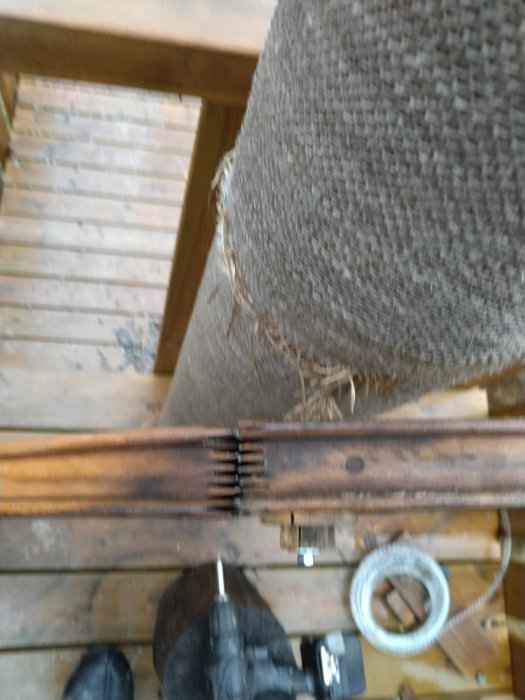 Reparation av spinnrockshjul med hålband på en träveranda, ovanifrån vy med synliga trägolv och verktyg.