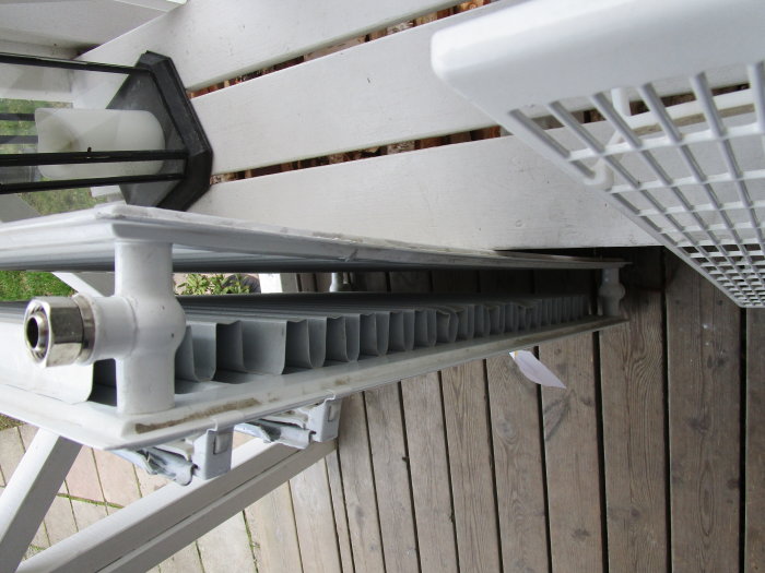Bild på en sönderfrusen radiator med två paneler och toppgaller, gulvit ton, placerad utomhus.