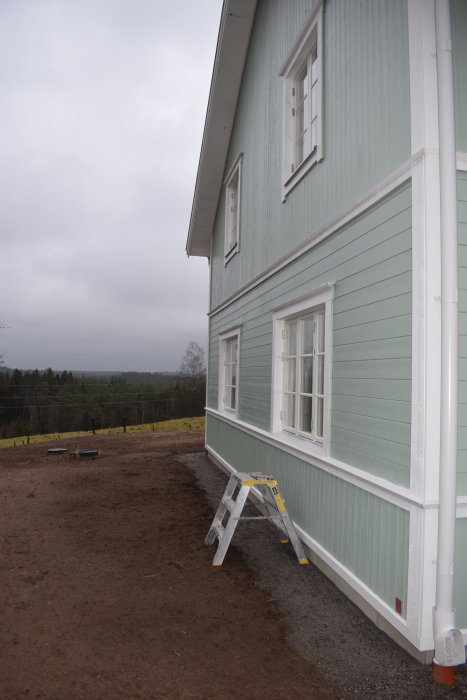 Husets hörn med fönster och stegar mot en nyfärdig fasad, inomhus städning pågår.