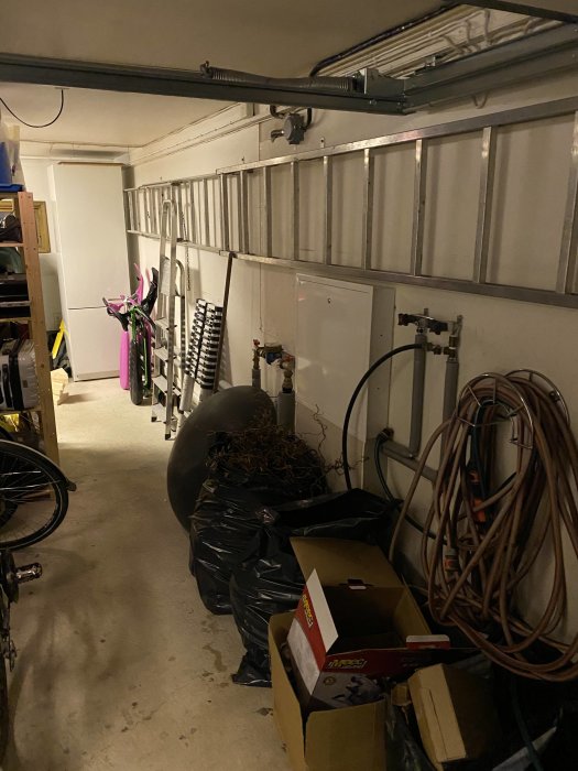 Garageinre med en öppen vägg som visar isolering och rör, cyklar och redskap lagrade längs väggen.