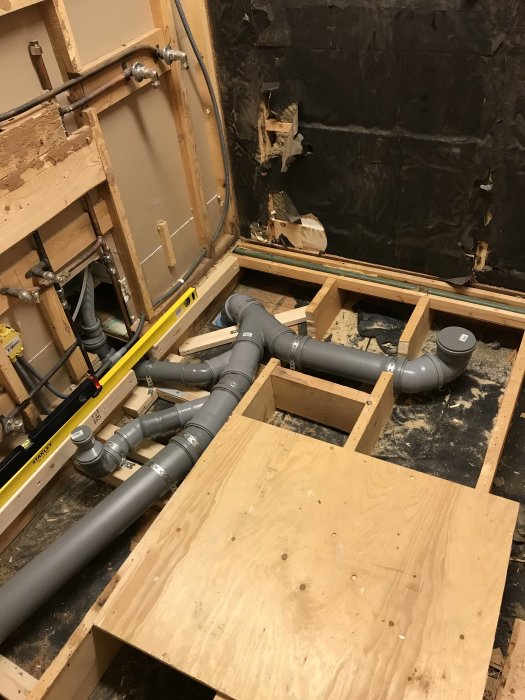 Gråa VVS-rörinstallationer i en byggkonstruktion med en 87-graders böjning, avstött med trä och verktyg synliga.