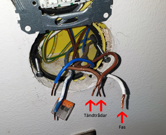 Elinstallation med öppen dosa som visar fas- och tändtrådar, markerade med text, ej inkopplade.