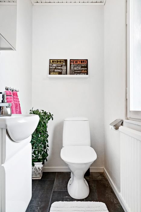 Vit gästtoalett med laminatgolv, vattenradiator, handfat, toalett och väggdekor med stadsteman.
