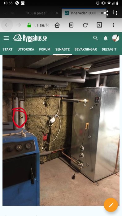 En källare med en blå panna, rörledningar och en markerad ventil på en stenmur.