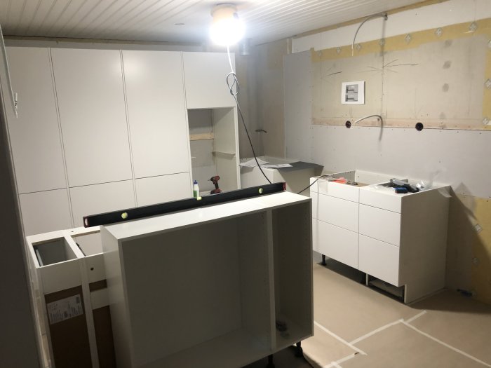 Kök under renovering med vita skåp, väggar förberedda för kakel och verktyg synliga.