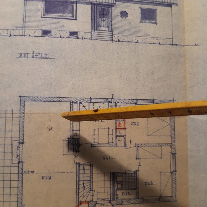 En hand som håller en linjal mot en arkitektonisk ritning med en planlösning och en husfasad.