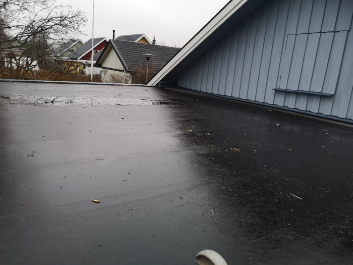 Läckage på platt garagetak med synlig vattenansamling nära byggnadens fasad.