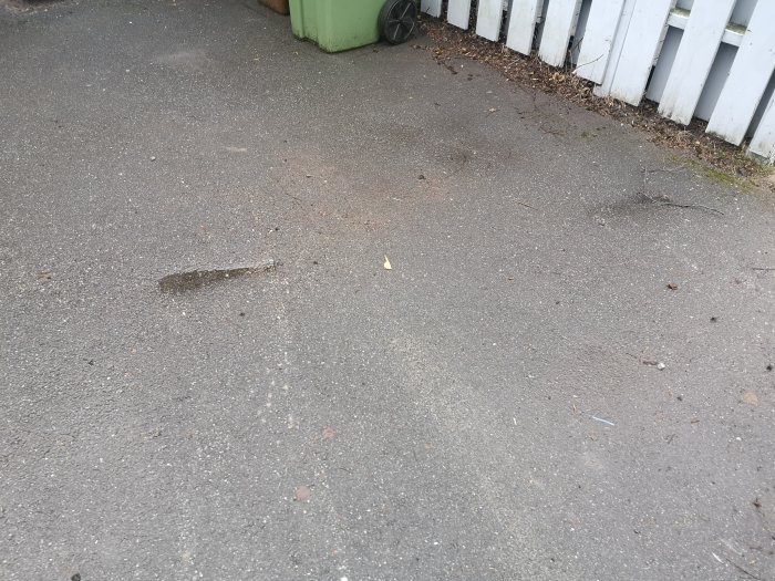 Asfaltsyta med försänkningar och repor på en garageuppfart, skador efter container.